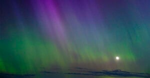 A breathtaking view of the Northern Lights displaying vibrant green and purple hues in the night sky, with a bright full moon illuminating the scene.