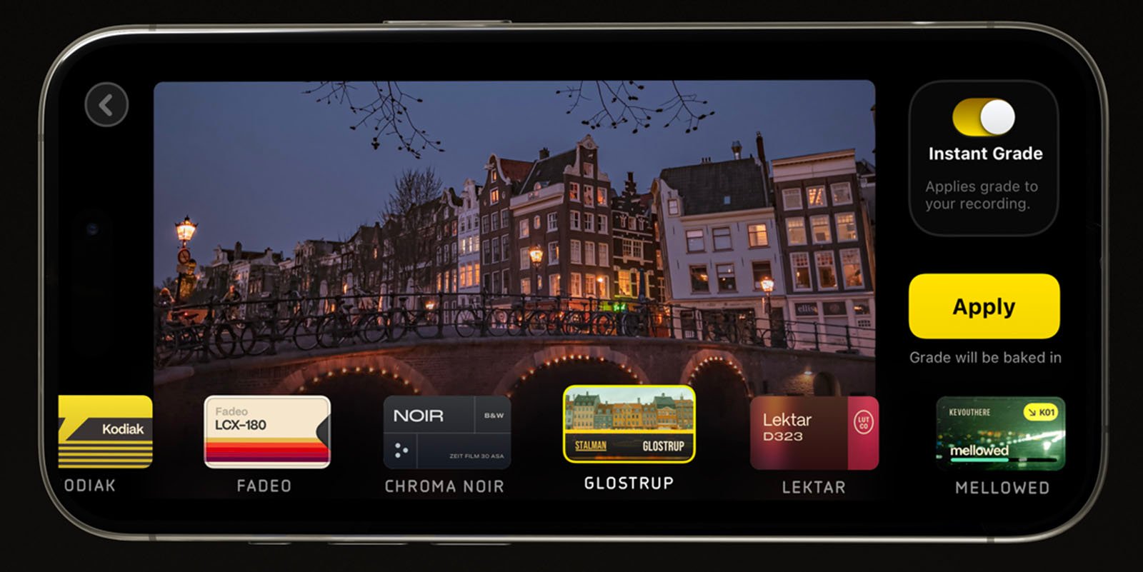 A smartphone screen displays a photo editing app with a picture of a canal and buildings at dusk. Various filter options are visible below the image, including Kodinek, Fadeo, Chroma Noir, Glostrup, Lektar, and Mellowed. An "Instant Grade" toggle switch and "Apply" button are on the right.