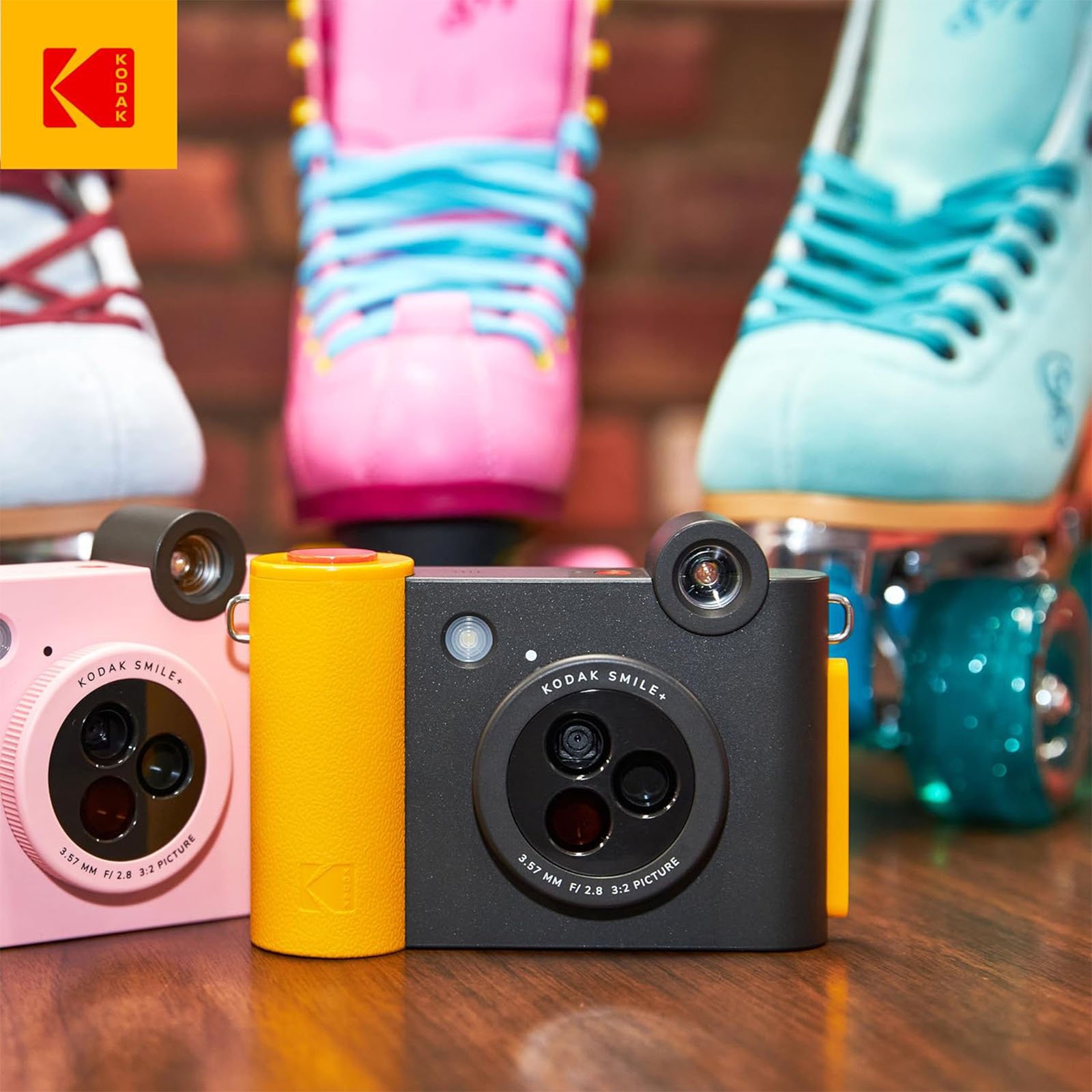 Three colorful Kodak Smile instant print cameras in pink, yellow, and blue, displayed on a table with patterned roller skates and teal mugs in the background.