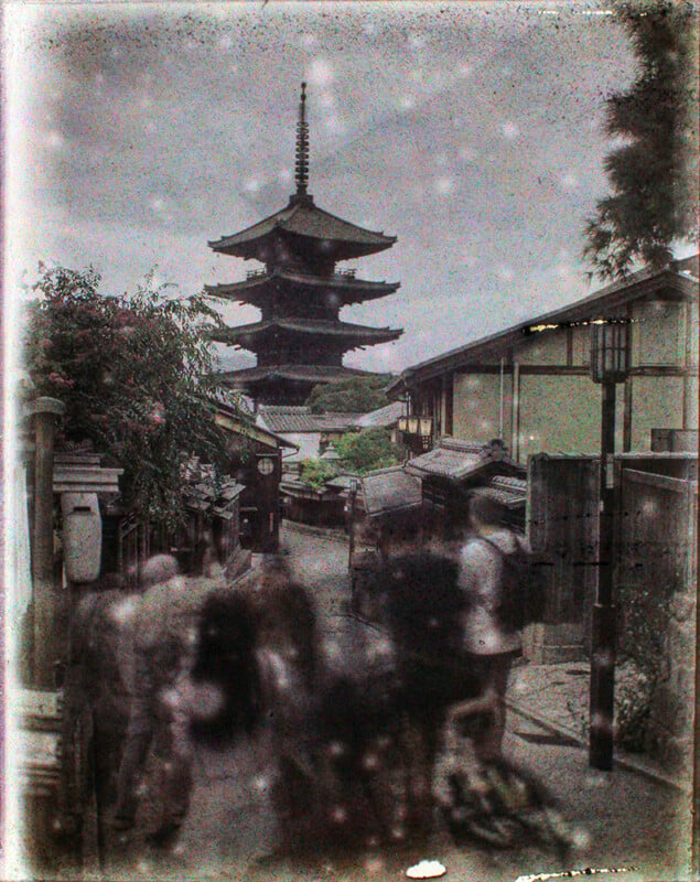 An aged photo depicting a traditional japanese pagoda with multiple tiers, visible through a street lined with quaint houses, under a faded, speckled sky, suggesting an antique or historical ambience.