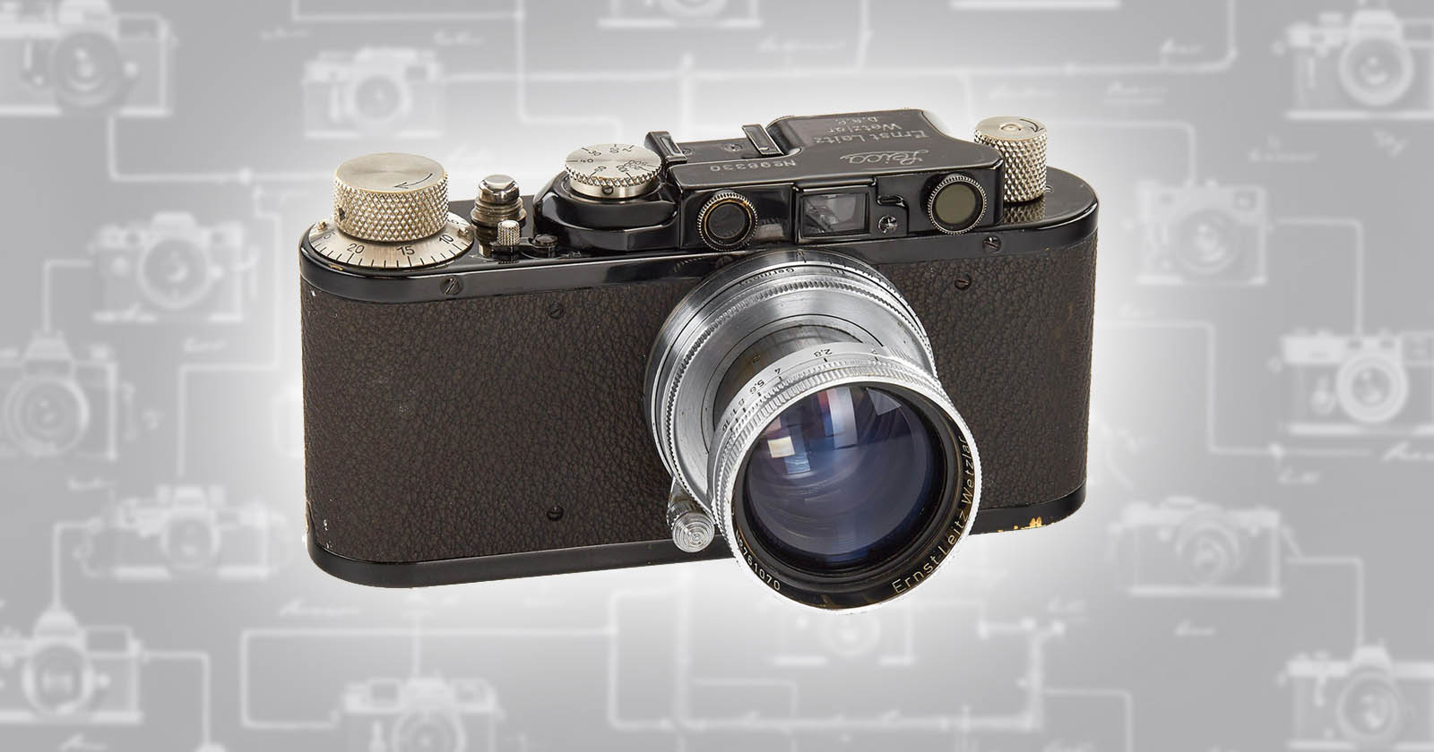 A vintage black camera with a large silver lens is displayed against a gray background featuring faint outlines of various camera models. The camera has several dials and buttons on its top surface. The lens is prominently extended towards the viewer.
