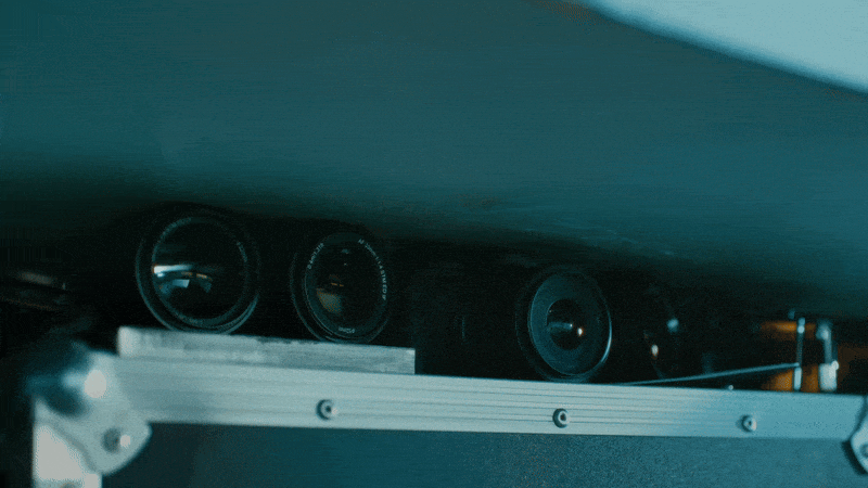 Close-up view beneath a piece of machinery showing three black, cylindrical rollers arranged in a line, all partially illuminated by a blue light.