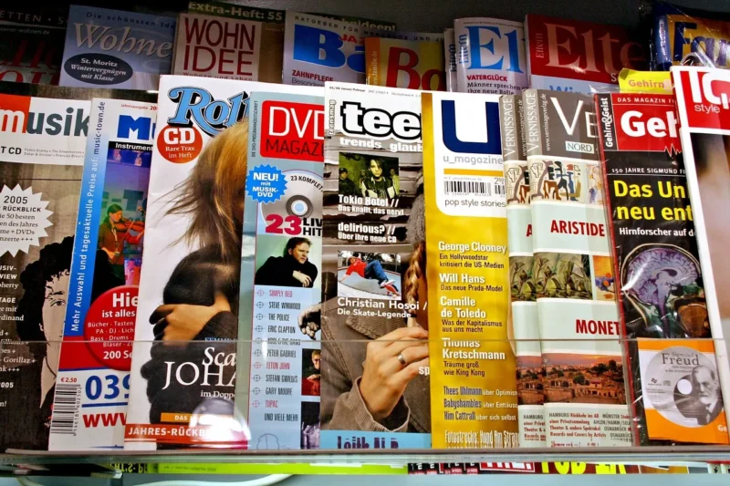 A diverse array of magazines displayed on a rack, featuring a mix of titles and topics in various languages, with vibrant colors and prominent images on the covers.