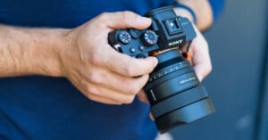 A person holding a sony camera with a zeiss lens, adjusting settings on the dial with their right hand. focus is on the camera, showing details of the buttons and lens.