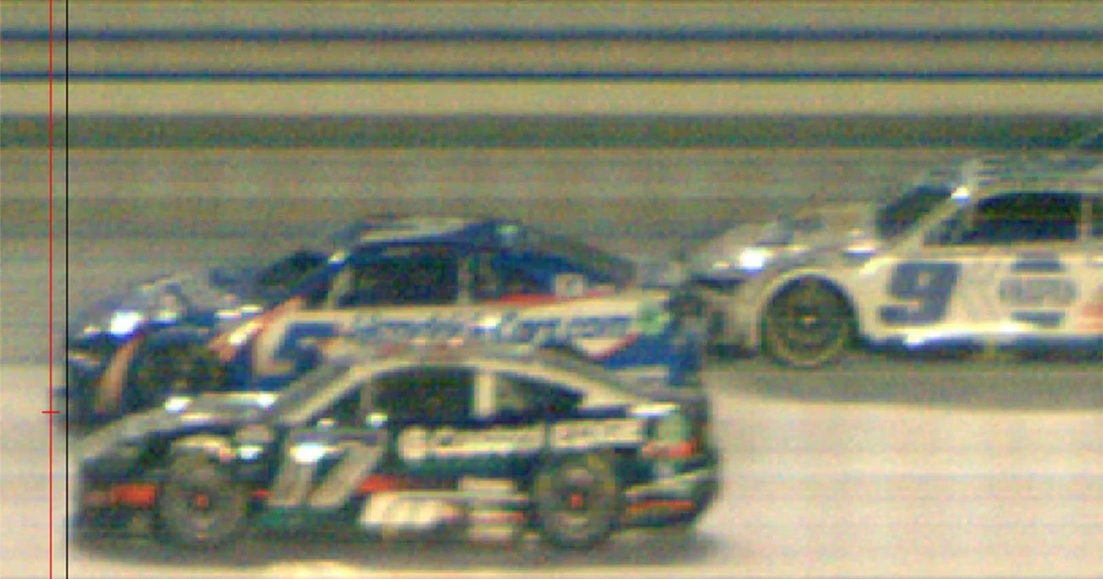 Blurry image of three race cars on a track, numbered consecutively, prominently displaying race decals and colors, captured in motion under nighttime lighting.