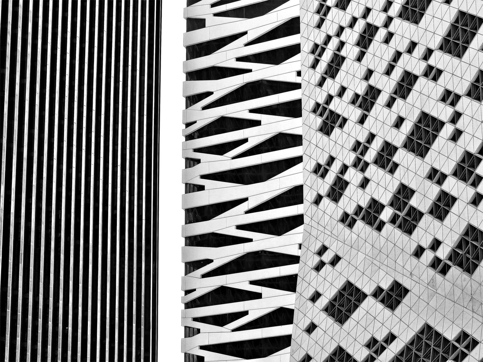 A black and white image featuring three modern high-rise buildings with distinct architectural designs. The left building has vertical stripes, the middle building has diagonal crisscross patterns, and the right building has an abstract, textured facade.