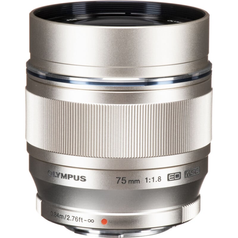 A silver olympus 75mm f/1.8 lens with msc branding, shown head-on against a white background. the focus and aperture rings are prominently displayed, featuring textured grips.