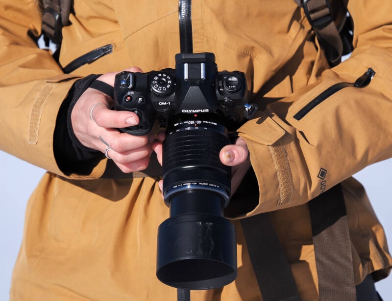 A person wearing a yellow jacket holds a dslr camera with both hands, ready to take a photo. the focus is on the camera and the photographer's hands.