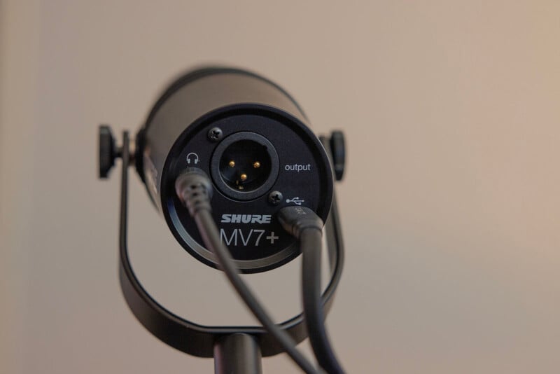 A close-up view of a shure mv7+ microphone, mounted on a stand, showing detailed ports and labels against a neutral background.