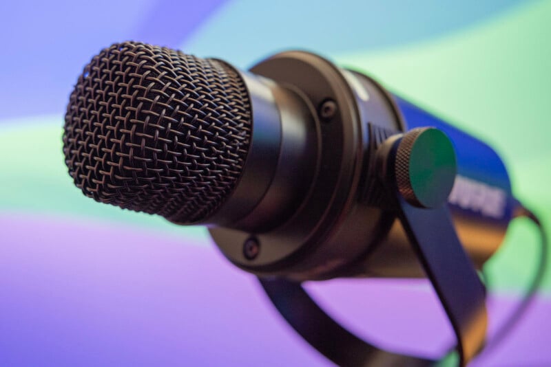 Close-up of a black dynamic microphone against a blurred background with colorful, swirling lights in hues of blue, green, and purple.
