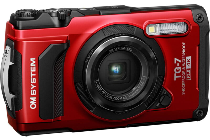 Red rugged waterproof digital camera with a prominent lens, flash, and labeled "om system tough tg-7." the camera is designed for durable and outdoor use.