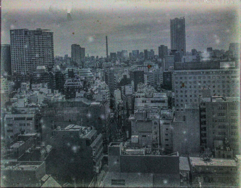 A grainy, vintage-style photo of a densely populated cityscape with a mix of mid-rise buildings under an overcast sky.