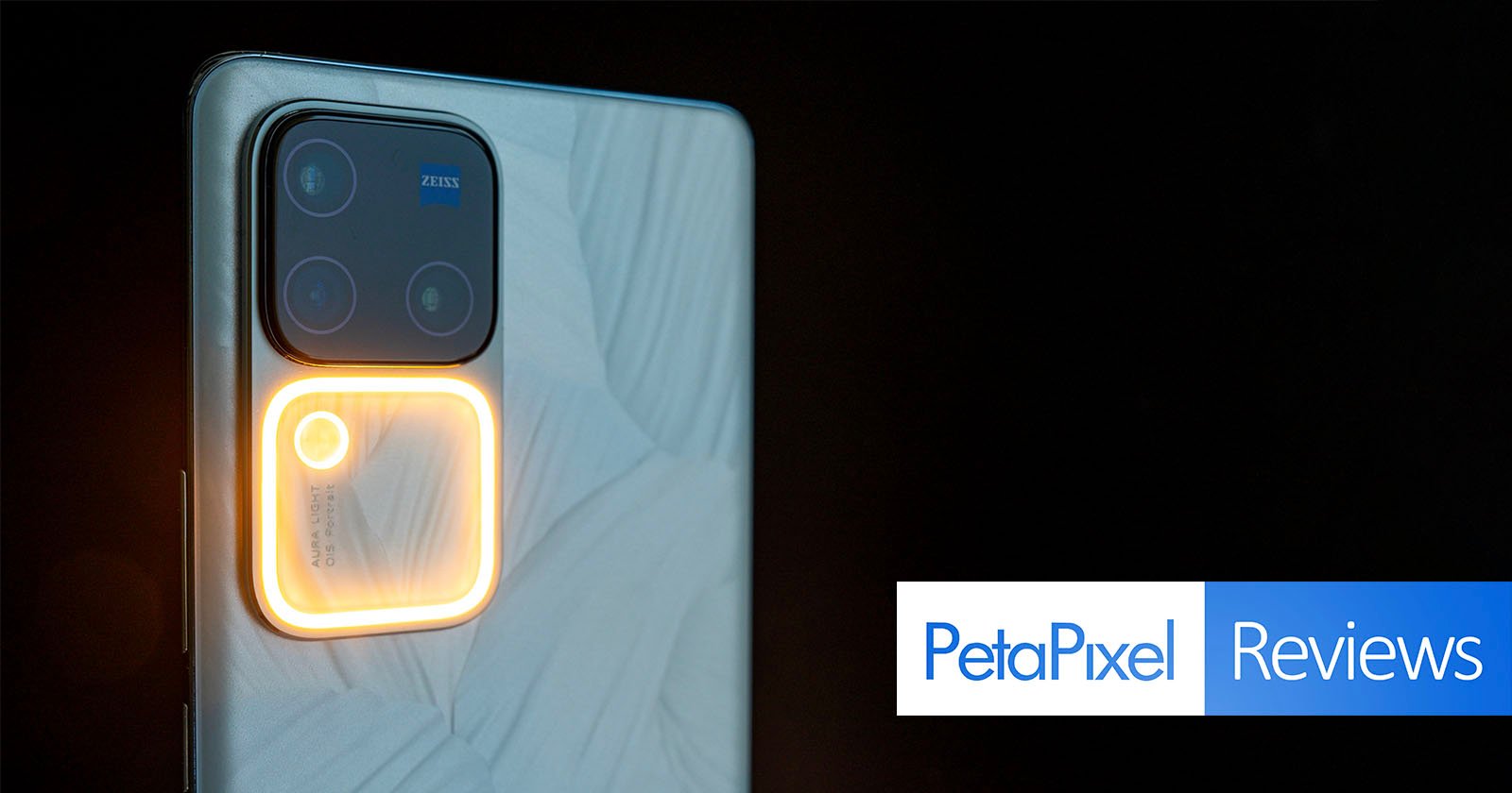A close-up of a smartphone with a sophisticated camera system, featuring a large lens with a glowing ring light, set against a dark background. the logo petapixel reviews is visible in the corner.