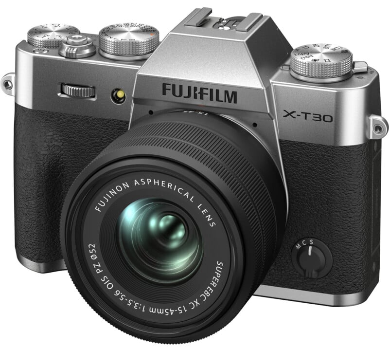 A fujifilm x-t30 camera with a silver top, black body, and mounted fujinon lens, sitting on a white background. the camera is viewed from the front-left angle.