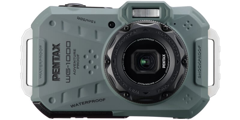 A rugged, grey Pentax WG-1 adventure-proof digital camera is shown from the front. The camera features a waterproof and shockproof design with various buttons and a lens in the center. The model and brand names are prominently displayed on the body.