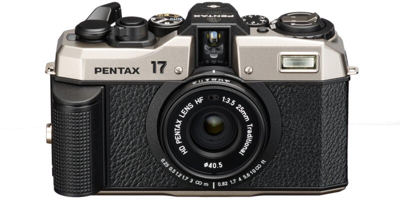 A retro-style Pentax 17 camera with a black and silver body. The camera has a large central lens labeled "HD Pentax Lens HF 1:3.5 25mm Traditional" and several control dials and buttons on the top. The front features textured grip areas and a built-in flash.