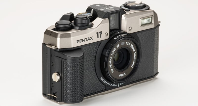 A silver and black Pentax 17 camera with a 12.5mm f/3.5 lens is shown against a white background. The camera has a textured grip, multiple control dials on the top, a viewfinder, and a flash on the front right section above the lens.