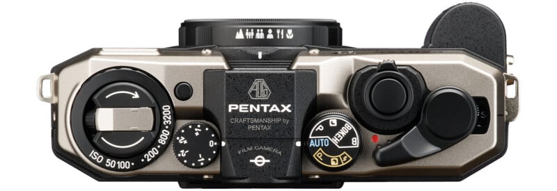 A top-down view of a Pentax film camera featuring various dials, a shutter button, and an ISO setting range from 50 to 3200. The camera body is silver with black accents, and the branding "Pentax" is prominently displayed in the center.