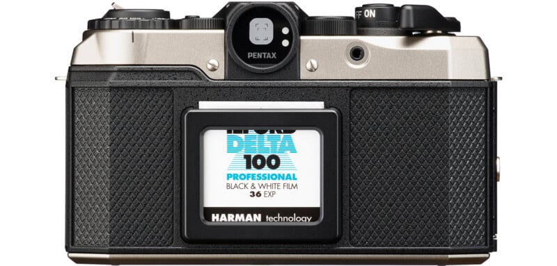 A vintage Pentax film camera with a roll of Ilford Delta 100 Professional black and white film loaded. The camera has a textured black grip and metallic upper body, with various buttons and dials visible on top.