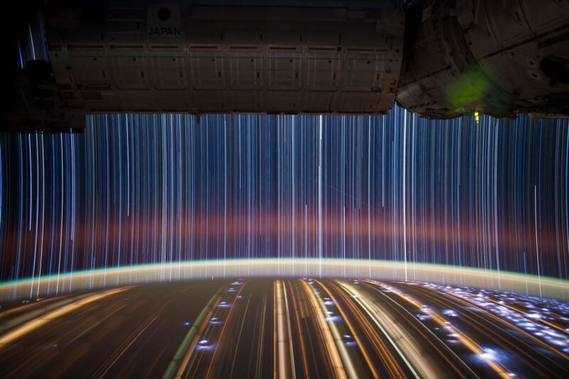 A stunning view from the International Space Station shows streaks of light from stars and city lights on Earth beneath the horizon. The image captures the curvature of Earth with layers of atmospheric colors transitioning from blue to orange.