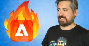 A man with a beard and gray streaked hair looks uneasy and frowns at a stylized, pixelated flame icon featuring the Adobe logo against a blue, pixelated background. He is wearing a black t-shirt with a pixelated character design.
