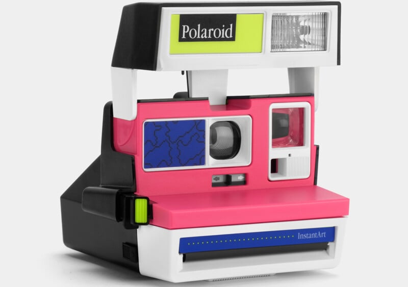 A retro Polaroid instant camera with a vibrant pink front panel, blue geometric design, and white and black detailing. The camera features a built-in flash, viewfinder, and various buttons. A green label with "Polaroid" is on the flash housing.