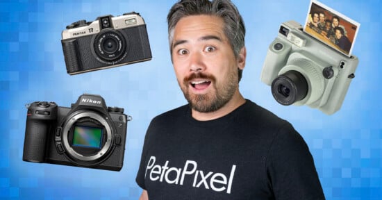 A man with a surprised expression, wearing a black "PetaPixel" shirt, is in front of a blue checkered background. Floating around him are three cameras: an old Pentax film camera, a modern Nikon DSLR, and a Polaroid instant camera with a printed photo.

.