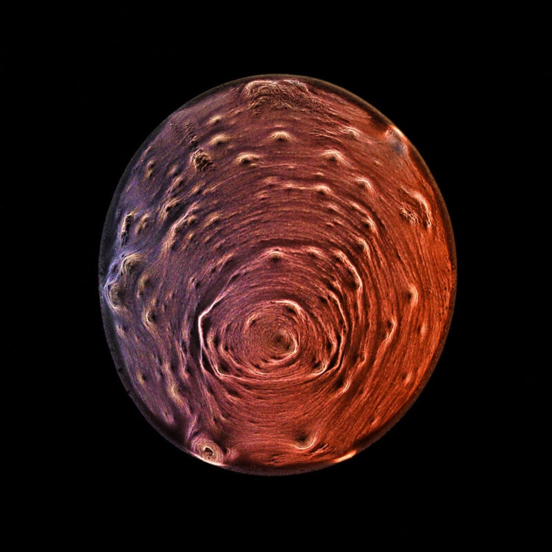 Image of Jupiter's North Pole taken by NASA’s Juno spacecraft. The image shows a circular view of the planet with a swirling atmospheric pattern in shades of red, purple, and orange, depicting cyclones and gas storms against the blackness of space.