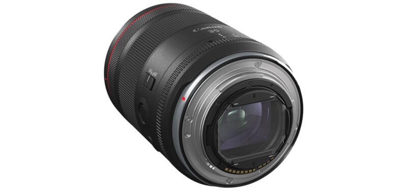 A close-up view of a Canon camera lens. The lens features assorted switches and markings and is mostly black with a red accent ring near the end. The inner glass elements and electronic contacts on the mounting side are visible.