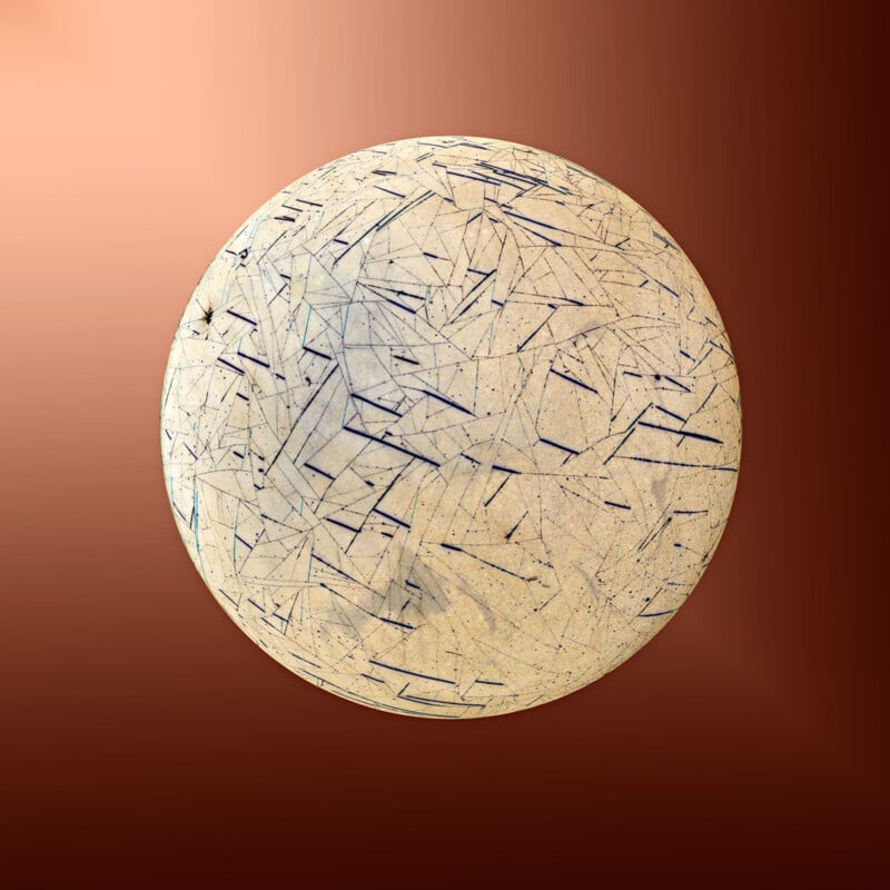 A circular object with a pale, beige surface covered in a complex network of thin, dark, intersecting lines, set against a gradient background transitioning from light to dark brown tones. The object appears textured and detailed with an abstract pattern.