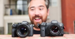 A bearded man with short hair is smiling excitedly behind two cameras placed on a brick surface. The camera on the left is a Sony Alpha series, and the one on the right is a Canon EOS R5. Both cameras have large lenses facing forward.