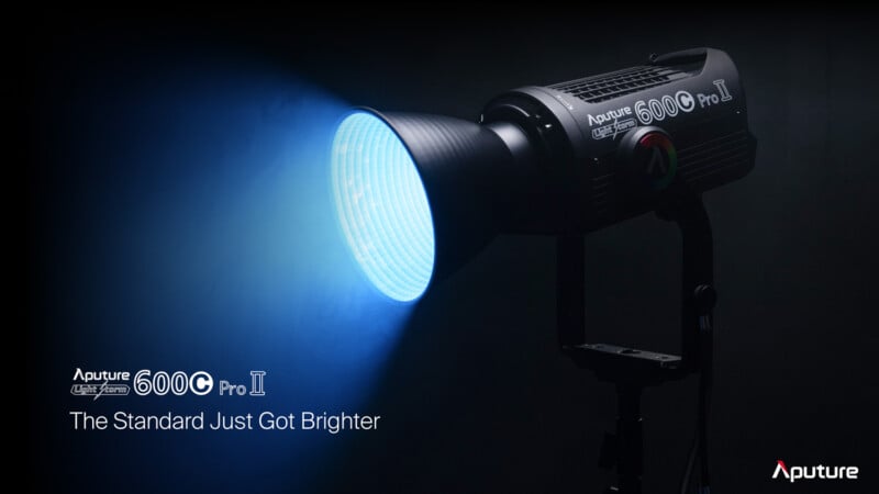 A professional lighting unit, Aputure 600C Pro II, shines a bright blue beam in a dark setting. The text reads "Aputure 600C Pro II - The Standard Just Got Brighter." The unit is mounted on a stand with visible branding and control buttons.