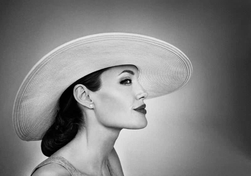 A black and white profile photo of a woman wearing a large, wide-brimmed hat. She has dark, styled hair and is looking to the right with a serene expression. The lighting highlights her facial features, giving the image a classic, timeless feel.