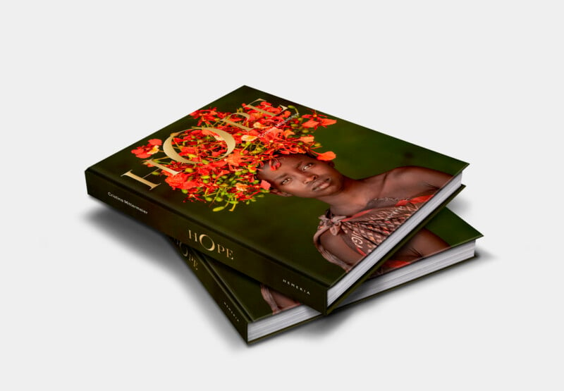 Two hardcover books titled "HOPE" are stacked, with the top book slightly offset. The cover features a photograph of a person adorned with vibrant orange flowers on their head and shoulders against a green background. The word "HOPE" is prominently displayed in large, golden letters.