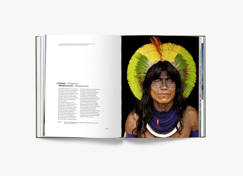 Open book displaying a magazine article on the left page with text and a large portrait of a person with long hair, face paint, colorful tribal headdress, and traditional neck adornments on the right page. The background is solid black.