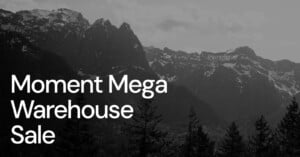 A grayscale image of a mountainous landscape, featuring dense forests and rugged peaks under a cloudy sky. Bold white text on the left side reads, "Moment Mega Warehouse Sale.
