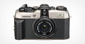 A silver and black Pentax 17 camera with a retro design is displayed. It features a prominent viewfinder, various control dials, and a lens marked "HD Pentax-DA 25mm f/3.5." The camera has a textured grip on the front for comfortable handling.