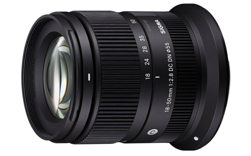 A black Sigma zoom lens with a focal length range of 18-50mm, an aperture of f/2.8, and DC DN technology for crop sensor mirrorless cameras. The lens has a ribbed focus ring and markings indicating focal lengths and aperture settings in white text.