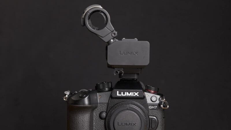A black Panasonic Lumix GH7 camera with a light mount attachment on top is set against a plain black background. The camera's brand and model name, "Lumix GH7," are clearly visible above the lens.