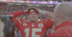 Patrick Mahomes wearing a red jersey with the number 15, and a red headband, looks joyful with his hands on his head amid a crowd in a stadium. The scoreboard in the background shows the 49ers 22 and Chiefs 25, suggesting a victory celebration.