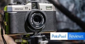 A close-up shot of a vintage Pentax camera on a tripod with a waterfall in the blurred background. The camera's branding and lens details are clearly visible. Overlaid at the bottom right is the "PetaPixel Reviews" logo.