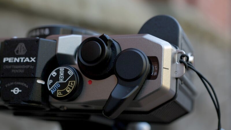 Close-up shot of a Pentax film camera, showing the top section with various controls. The view includes the shutter speed dial, film advance lever, and part of the camera body, showcasing intricate details and craftsmanship.