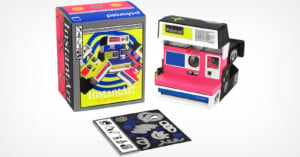 Image of a Polaroid camera and its packaging. The camera is pink, black, and white with a flash unit and color film inside. Next to it is the product box with vibrant designs, and in the foreground, there are various stickers and decals for customization.