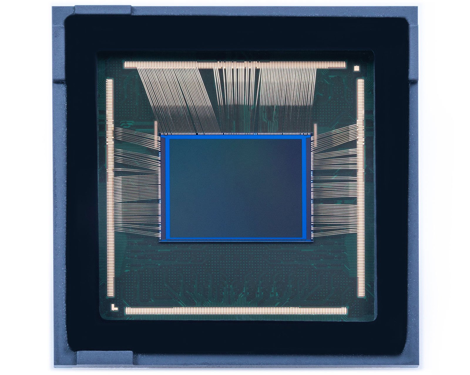 Close-up view of a semiconductor chip with visible wiring connections. The square black and green structure has fine gold wires extending from its edges to the surrounding frame. The central area is flat and framed with a blue outline.