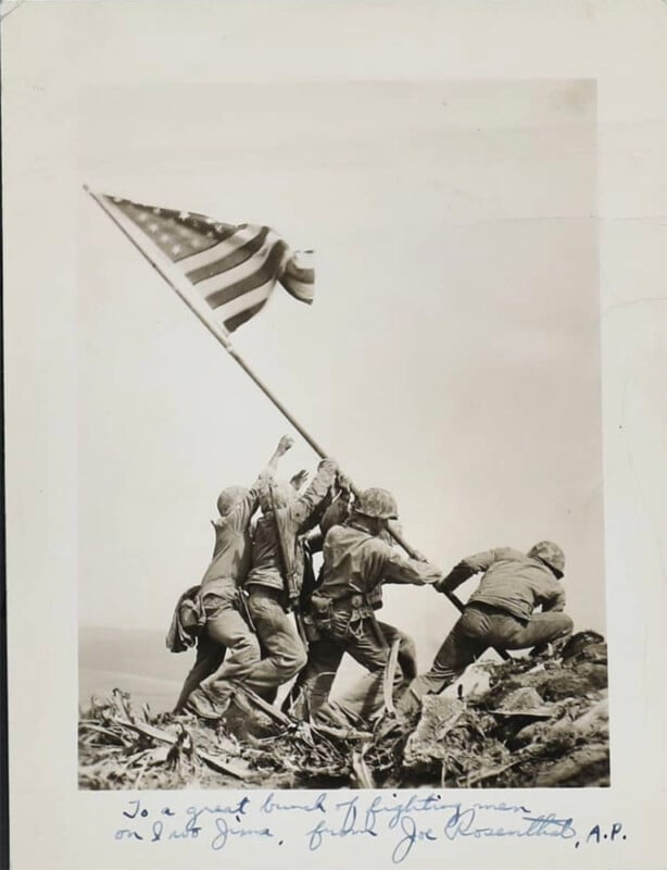 A black-and-white photo shows several soldiers raising an American flag atop Mount Suribachi during the Battle of Iwo Jima. Handwritten text appears at the bottom, and debris is scattered on the ground.
