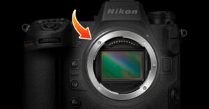 A close-up view of a Nikon Z series mirrorless camera body. The image highlights the lens mount and sensor area with an orange arrow pointing towards it, emphasizing the central feature of the camera. The camera buttons and grip are also visible.