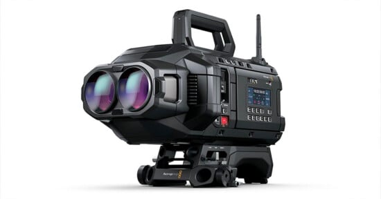 A high-tech, black electronic device resembling a large camera with an ergonomic handle on top. It has dual lenses on the front and a display screen with numerous buttons on the side. It is mounted on a robust, adjustable base.