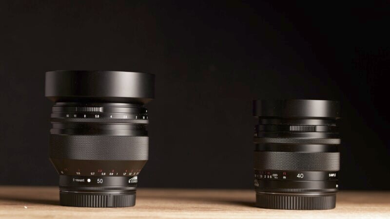 Two camera lenses are placed on a wooden surface with a black background. The lens on the left is larger with a 50mm focal length, while the lens on the right is smaller with a 40mm focal length. Both lenses have black exteriors and detailed focus rings.
