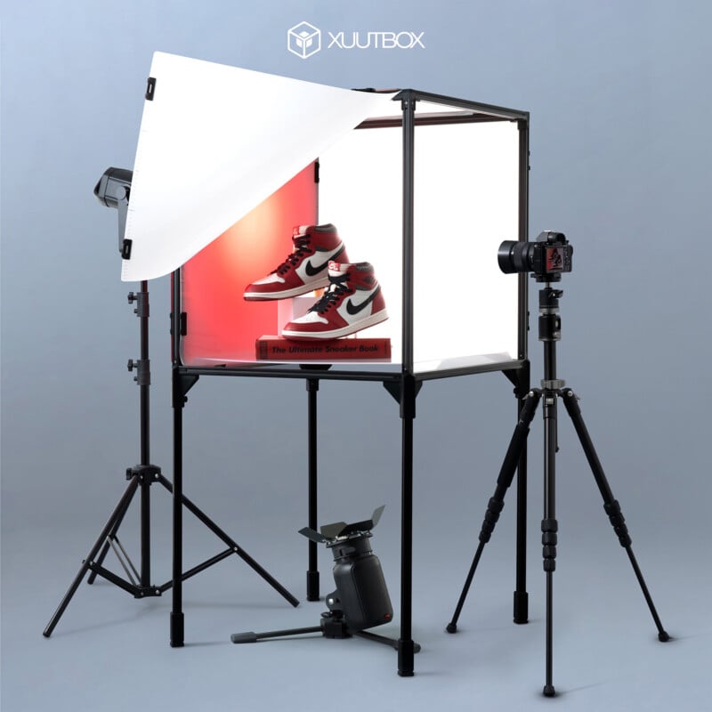 A photography setup featuring a pair of red and white sneakers with black accents displayed inside a lightbox. Two camera tripods and several studio lights surround the lightbox. The logo "Xuutbox" is visible at the top of the image.