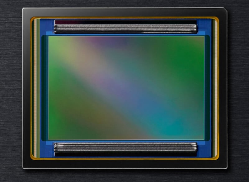 A close-up image of a digital camera sensor with a vibrant, multicolored surface, encased in a rectangular frame with a gray metallic border. The sensor features two cylindrical components, one on the top and one on the bottom.